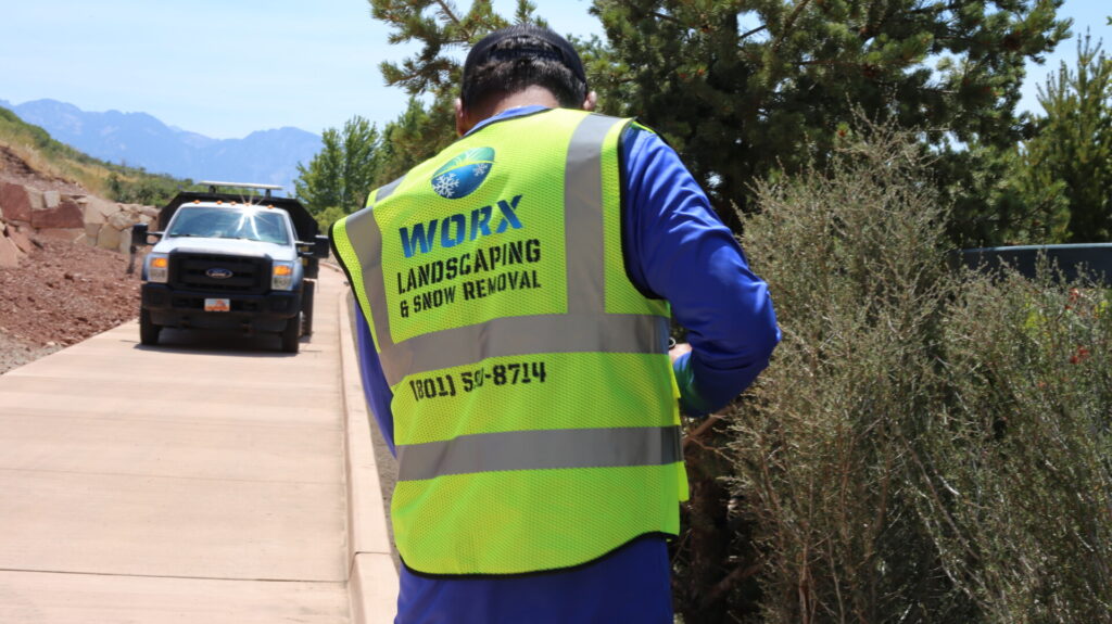 Landscaper in high-visibility vest near truck on road.