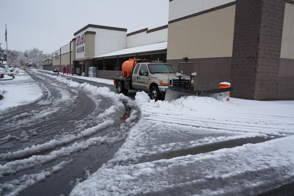 Snowplow clears parking lot in front of store.