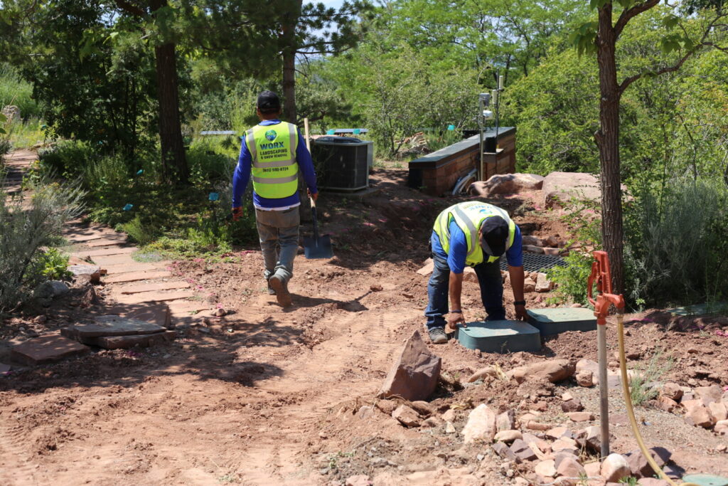 Workers landscaping a garden pathway with tools.
