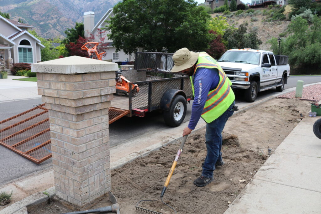 Worker landscaping with rake beside trailer and truck.