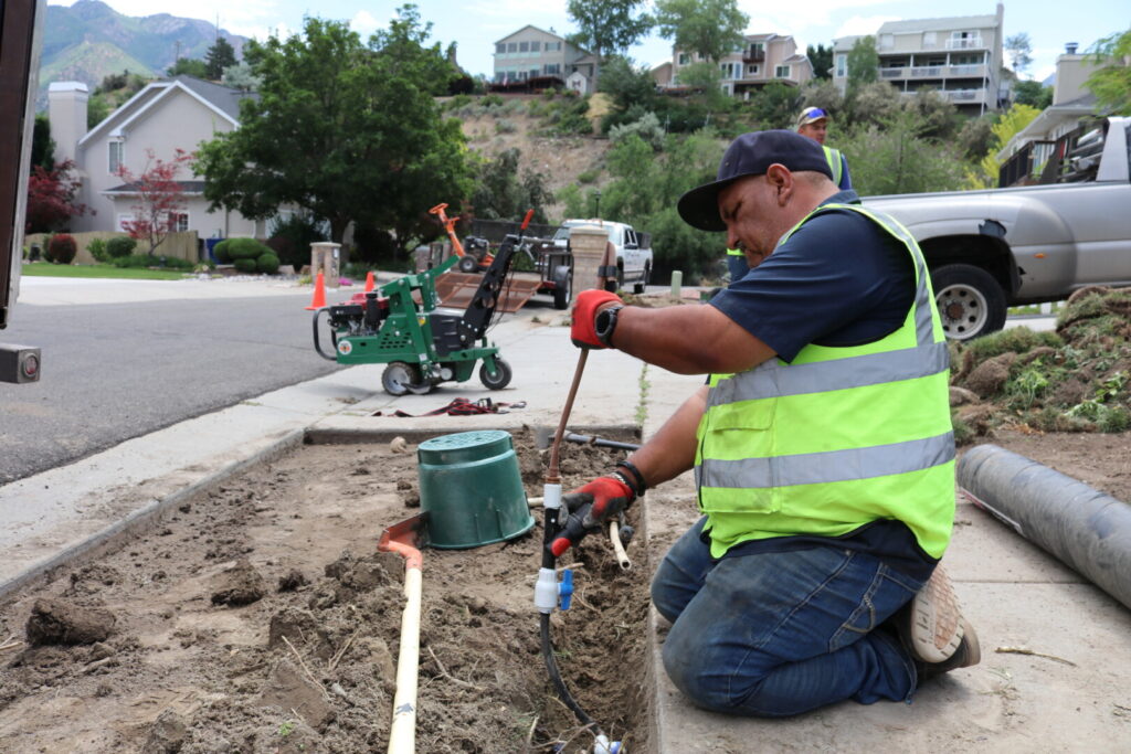 Worker repairs underground pipes on a suburban street.