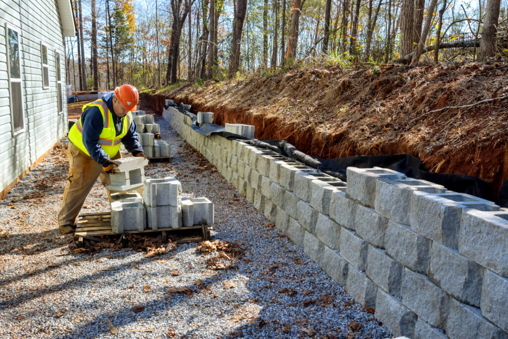 Worker building stone retaining wall at construction site.