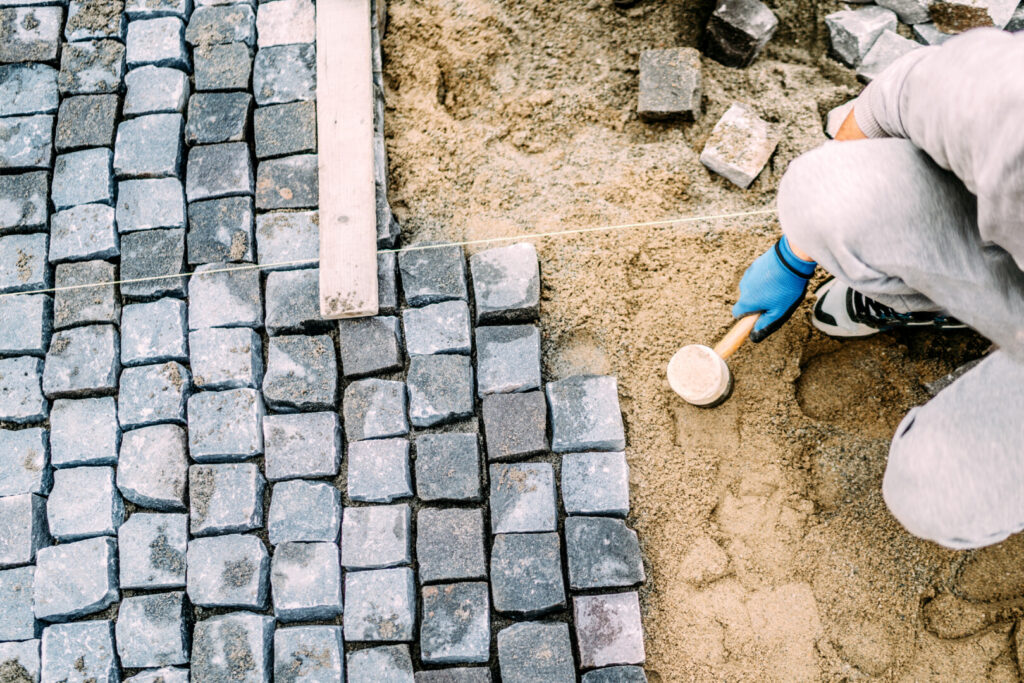Worker placing cobblestones on sandy ground.