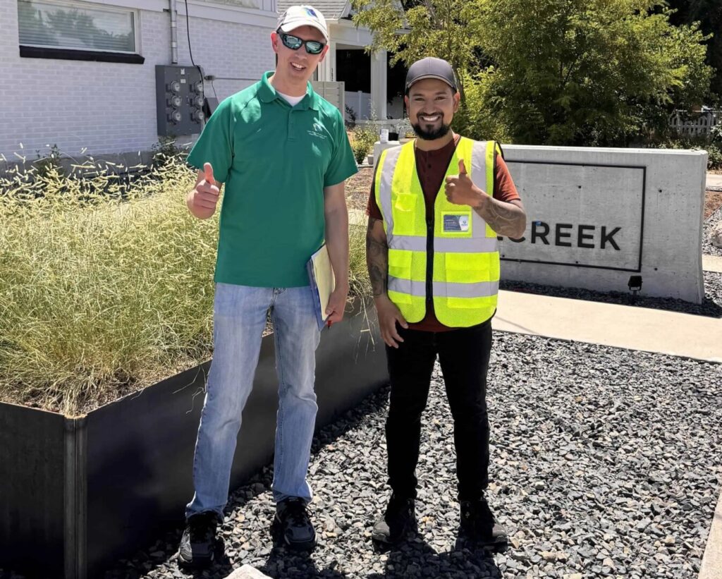 Two workers smiling, outdoor landscaping project.